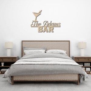 May include: A wooden sign with a martini glass and the text "The Adams BAR" above a bed with a gray duvet cover and two nightstands.