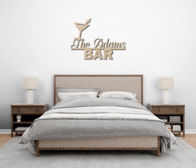 May include: A wooden sign with a martini glass and the text "The Adams BAR" above a bed with a gray duvet cover and two nightstands.