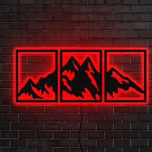 Pu&ograve; includere: Tre immagini di silhouette di catene montuose nere in cornici al neon rosso su un muro di mattoni neri.