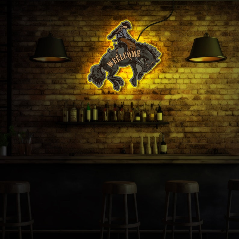 Op de afbeelding: Neon-bord met een cowboy die op een paard rijdt en het woord "WELCOME" in vintage stijl. Het bord hangt aan een bakstenen muur in een bar.