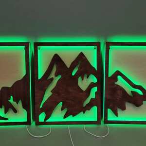 Pu&ograve; includere: Tre pezzi di arredamento da parete in legno con un design a silhouette di montagna. Ogni pezzo ha una luce LED verde attorno al perimetro.