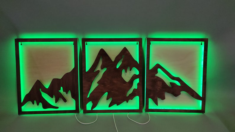 Pu&ograve; includere: Tre pezzi di arredamento da parete in legno con un design a silhouette di montagna. Ogni pezzo ha una luce LED verde attorno al perimetro.