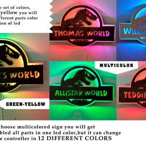 Op de afbeelding: Vier houten dinosaurusvormige borden met LED-verlichting. Elk bord heeft een andere naam: "Thomas World", "William World", "Samuele's World", "Allistar World" en "Teddie's World". De borden kunnen in groen en geel of in 12 verschillende kleuren worden verlicht met behulp van een afstandsbediening.