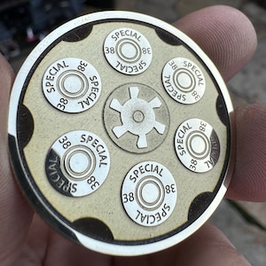 Könnte beinhalten: Ein runder, hölzerner Untersetzer mit silbernem Rand und einem Sternburst-Design in der Mitte. Sechs kugelförmige Kreise umgeben den Sternburst, jeder mit dem aufgedruckten Text "SPECIAL 38".