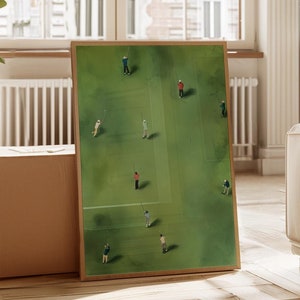 Puede incluir: Una pintura enmarcada de un campo verde con personas jugando a un juego. Las personas visten ropa de diferentes colores y están dispersas por el campo. La pintura está en un marco de madera y está colgada en una pared.