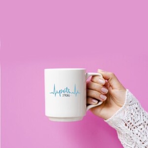 Puede incluir: Taza de cerámica blanca con un gráfico de latido del corazón azul y el texto "POTS STRONG".