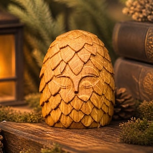 May include: A wooden owl sculpture with a textured, layered design. The owl is a warm, natural wood colour and sits on a wooden surface with moss and pinecones. A lit lantern and books are in the background.