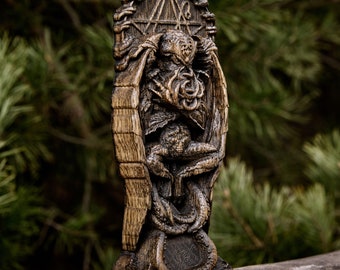 May include: A wooden carving of Cthulhu, a fictional cosmic entity from the works of H.P. Lovecraft, with tentacles and a humanoid form. The carving is set against a backdrop of green foliage.