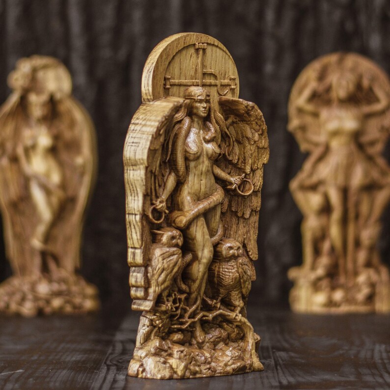 May include: A wooden sculpture of a female figure with wings, standing on a base with two owls. The figure is carved in a detailed style and has a natural wood finish.