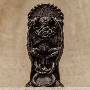 May include: A black resin statue of a creature with wings and tentacles, sitting on a throne with a circular design. The creature has a crown on its head and is holding its hands in front of its face.