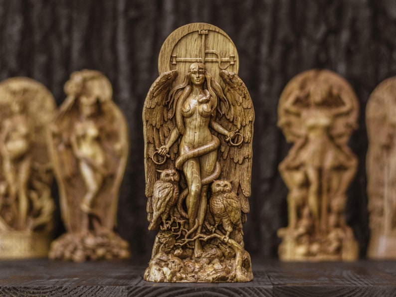 May include: A wooden sculpture of a woman with wings and a snake wrapped around her. She is standing in front of a wooden door with a cross on it. There are two owls on either side of her.