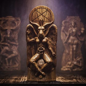 May include: A wooden sculpture of Baphomet, a goat-headed deity, with wings and a pentagram. The sculpture is carved in detail and stands prominently, with other blurred wooden sculptures in the background. The overall theme is related to occultism and spirituality.