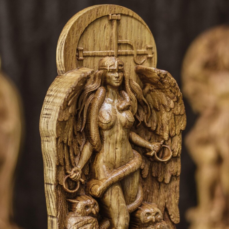 May include: A wooden sculpture of a winged female figure with a snake wrapped around her. The figure is standing on a base with two owls on either side. The sculpture is carved in a detailed and realistic style.