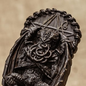 May include: A black and brown resin sculpture of Cthulhu, a fictional cosmic entity from the works of H.P. Lovecraft. The sculpture depicts Cthulhu with tentacles and wings, and is set against a background of a pentagram.