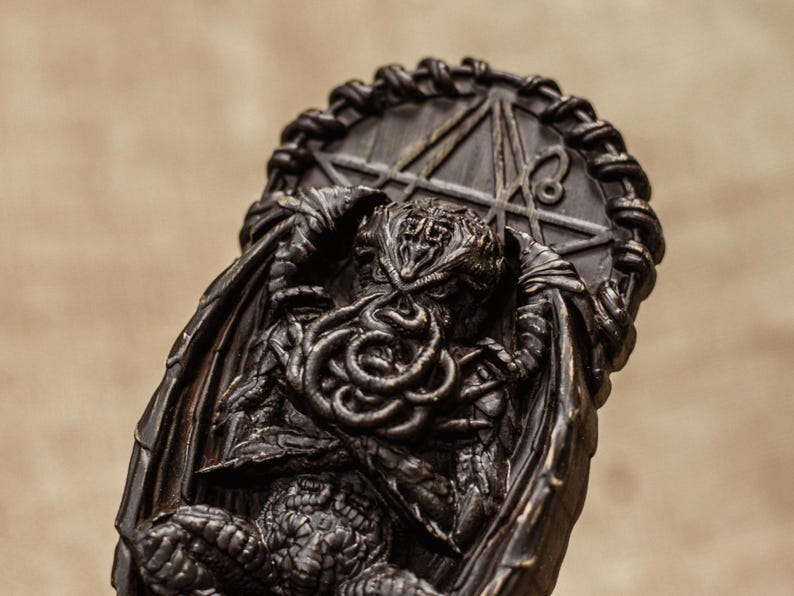 May include: A black and brown resin sculpture of Cthulhu, a fictional cosmic entity from the works of H.P. Lovecraft. The sculpture depicts Cthulhu with tentacles and wings, and is set against a background of a pentagram.