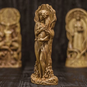 Puede incluir: Una escultura de madera de una mujer de pie en un &aacute;rbol, sosteniendo un animal peque&ntilde;o en sus brazos. La escultura est&aacute; tallada en un estilo detallado y tiene un acabado de madera natural.
