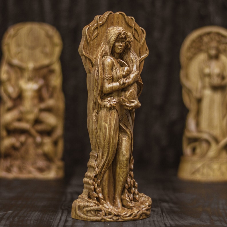 Puede incluir: Una escultura de madera de una mujer sosteniendo a un ni&ntilde;o peque&ntilde;o, ambas con detalles intrincados y un acabado de madera natural. La escultura est&aacute; colocada sobre un fondo oscuro.
