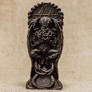 May include: A dark brown, detailed, sculpted figurine of Cthulhu, a fictional cosmic entity, with tentacles and wings. The figurine is standing on a base with a circular design.
