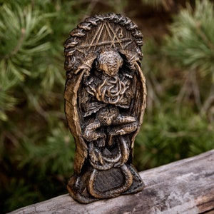 May include: A wooden sculpture of a creature with a human-like face and a body covered in vines. The sculpture is sitting on a throne with a pentagram design. The sculpture is painted in shades of brown and black.