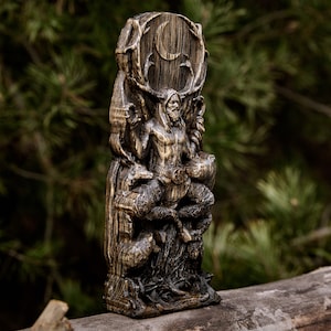 May include: A wooden carving of the Norse god Cernunnos, depicted as a horned figure with a beard, sitting on a throne with a crescent moon above him. He is surrounded by animals, including a deer and a wolf.
