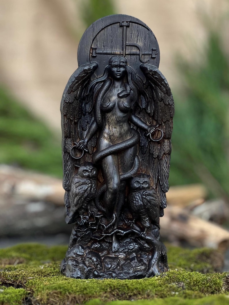 Puede incluir: Una estatua de madera negra de una figura femenina alada con una serpiente enroscada a su alrededor. Ella est&aacute; de pie sobre una base con dos b&uacute;hos a cada lado. La estatua est&aacute; tallada con intrincados detalles y tiene un acabado oscuro y envejecido.