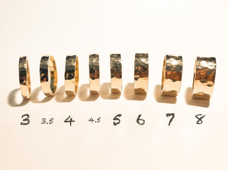 K&ouml;nnte beinhalten: Ein Satz von acht goldenen, geh&auml;mmerten Ringen in den Gr&ouml;&szlig;en 3 bis 8, auf einer wei&szlig;en Oberfl&auml;che angeordnet.