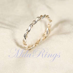 Peut inclure: Une bague argent&eacute;e et dor&eacute;e avec un motif torsad&eacute;. La bague pr&eacute;sente de petites pierres pr&eacute;cieuses transparentes et est pos&eacute;e sur un fond blanc cass&eacute;. Le texte "Mila Rings" est visible.