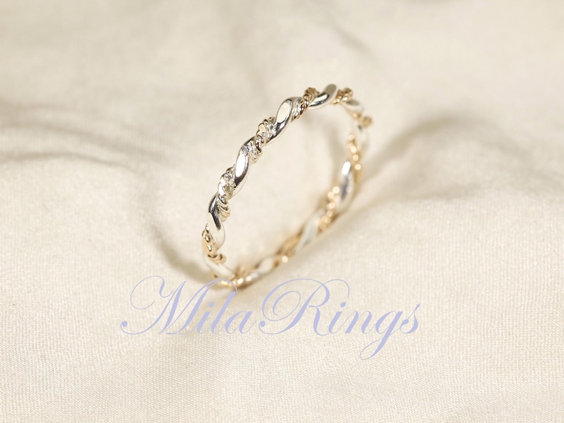 Peut inclure: Une bague argent&eacute;e et dor&eacute;e avec un motif torsad&eacute;. La bague pr&eacute;sente de petites pierres pr&eacute;cieuses transparentes et est pos&eacute;e sur un fond blanc cass&eacute;. Le texte "Mila Rings" est visible.