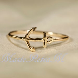 May include: A gold anchor ring. The anchor is a simple design with a ring that is thin and delicate.