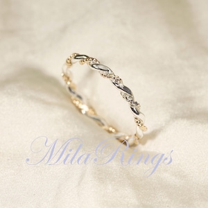 Peut inclure: Une bague torsad&eacute;e bicolore argent et or. La bague pr&eacute;sente un motif tress&eacute; avec des segments argent&eacute;s et dor&eacute;s altern&eacute;s. La bague est pr&eacute;sent&eacute;e sur une surface blanche textur&eacute;e. Le texte "Mila Rings" est visible.