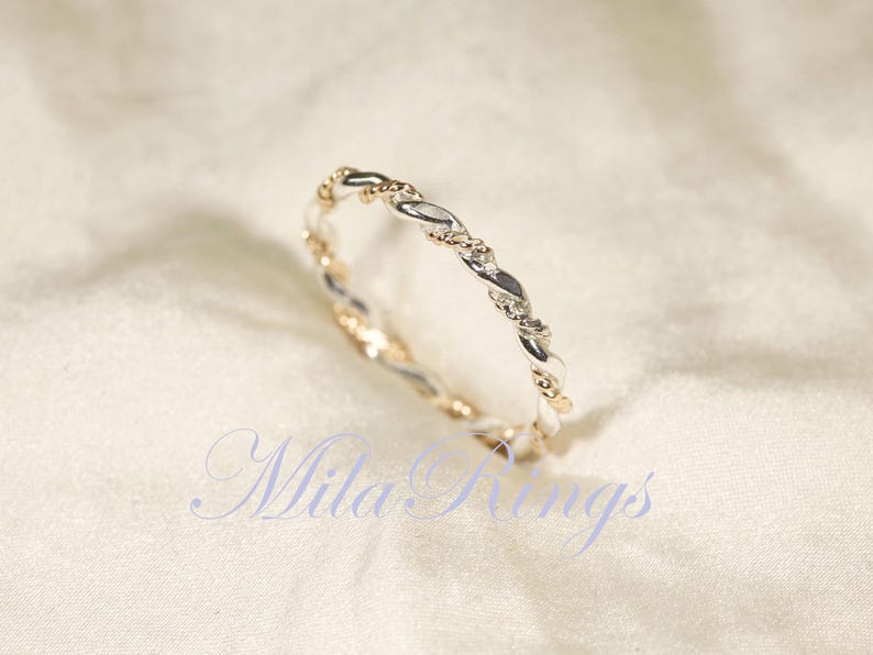 Peut inclure: Une bague torsad&eacute;e bicolore argent et or. La bague pr&eacute;sente un motif tress&eacute; avec des segments argent&eacute;s et dor&eacute;s altern&eacute;s. La bague est pr&eacute;sent&eacute;e sur une surface blanche textur&eacute;e. Le texte "Mila Rings" est visible.