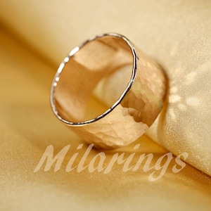 Op de afbeelding: Een gouden gehammerde ring met een brede band. De ring is gemaakt van metaal en heeft een getextureerd oppervlak.