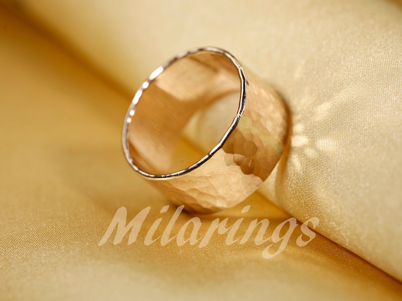 Op de afbeelding: Een gouden gehammerde ring met een brede band. De ring is gemaakt van metaal en heeft een getextureerd oppervlak.