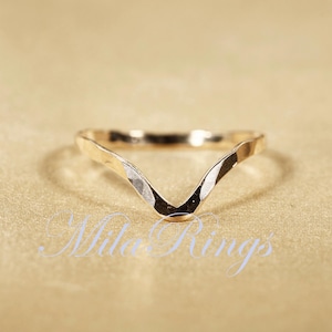 May include: A gold-toned, hammered metal ring with a V-shaped design. The ring is simple and elegant.