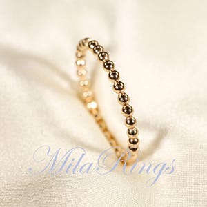 May include: A delicate gold ring with a beaded design. The ring is made of small, round beads that are evenly spaced along the band.
