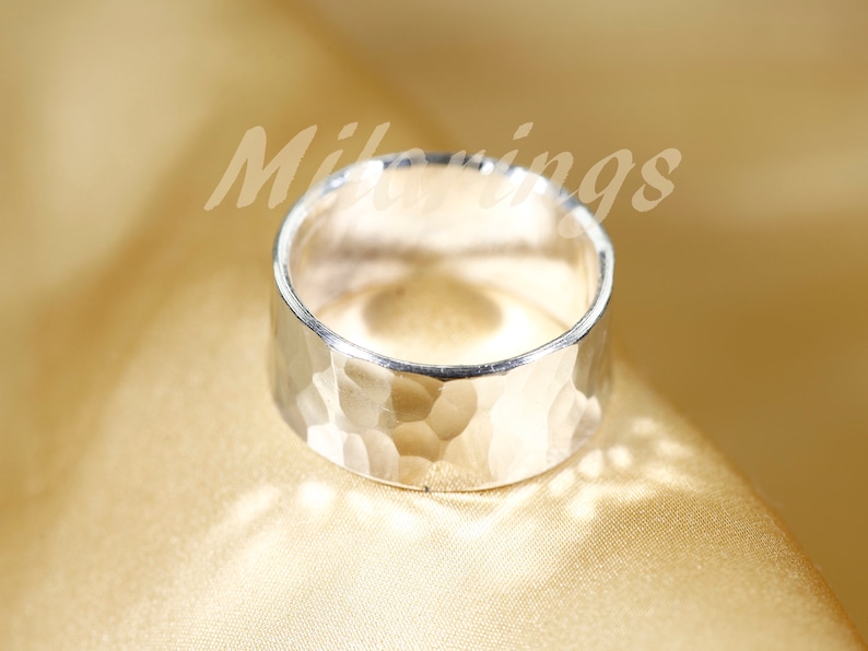 Op de afbeelding: Een zilveren gehammerde bandring. De ring is breed en heeft een getextureerd oppervlak.