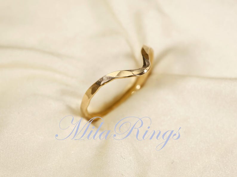May include: A gold, wavy, hammered ring. The ring is simple and elegant.