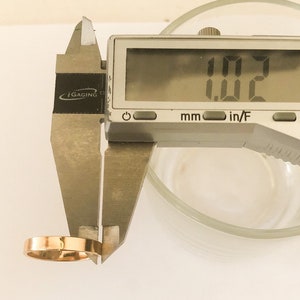 K&ouml;nnte beinhalten: Eine silberne digitale Schieblehre misst einen goldenen Ring. Die Schieblehre zeigt 0,02 Zoll an.