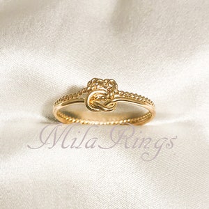 Könnte beinhalten: Ein goldener Knotenring mit einem zarten Seil-Design. Der Ring ist schlicht und elegant und perfekt für den Alltag.
