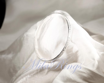 May include: A silver bangle bracelet with a delicate etched design. The bracelet is on a white fabric background.