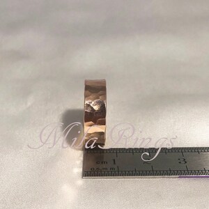 May include: A hammered rose gold band ring with a textured surface. The ring is measured against a ruler with markings in centimeters.