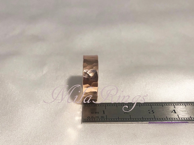 May include: A hammered rose gold band ring with a textured surface. The ring is measured against a ruler with markings in centimeters.
