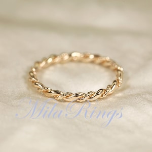 Peut inclure: Une bague dor&eacute;e avec un motif de corde torsad&eacute;e. La bague est circulaire et repose sur une surface douce et blanc cass&eacute;. Le design de la bague est un motif continu de brins entrelac&eacute;s.