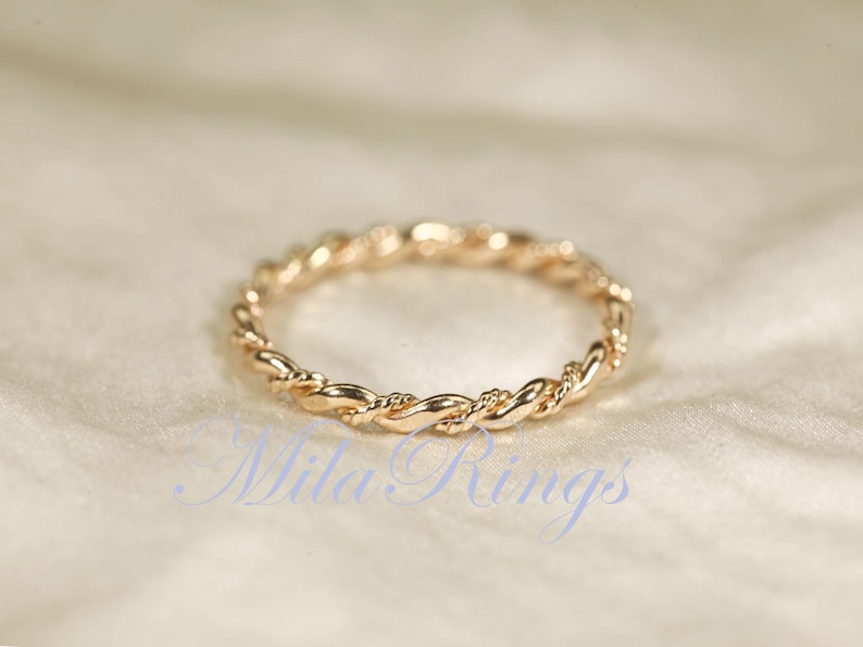 Peut inclure: Une bague dor&eacute;e avec un motif de corde torsad&eacute;e. La bague est circulaire et repose sur une surface douce et blanc cass&eacute;. Le design de la bague est un motif continu de brins entrelac&eacute;s.