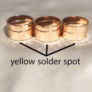 May include: Three gold hammered rings stacked on top of each other. The rings are soldered together and there is a small yellow solder spot visible on the bottom ring.