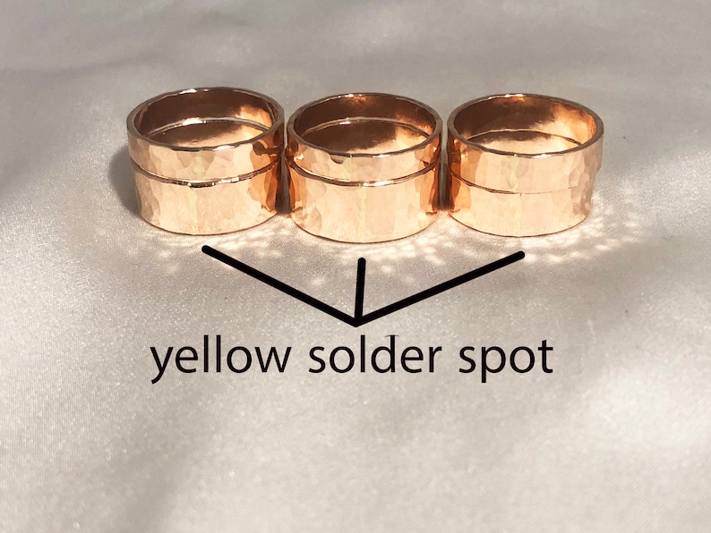 May include: Three gold hammered rings stacked on top of each other. The rings are soldered together and there is a small yellow solder spot visible on the bottom ring.