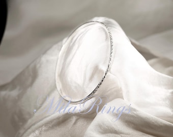 May include: A silver bangle bracelet with a textured design. The bracelet is on a white fabric background.