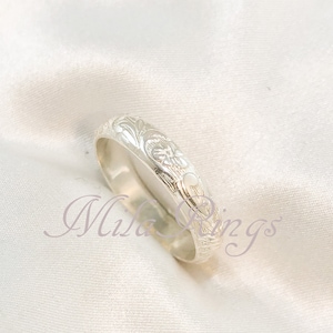 May include: A silver ring with an intricate floral design. The ring is on a white fabric background.