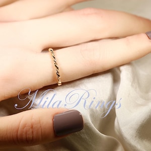 Peut inclure: Une bague dor&eacute;e avec un motif de corde torsad&eacute;e est port&eacute;e au doigt. La bague est d&eacute;licate et &eacute;l&eacute;gante. Le fond est de couleur neutre et douce. Le texte "Mila Rings" est visible dans l'image.