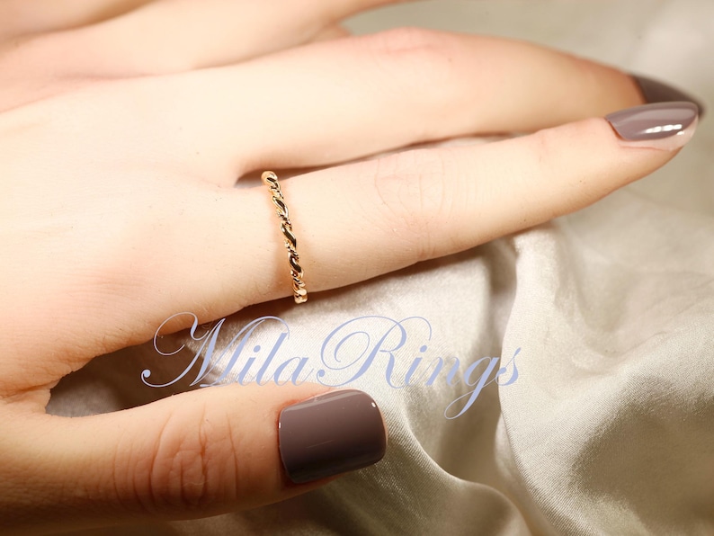 Peut inclure: Une bague dor&eacute;e avec un motif de corde torsad&eacute;e est port&eacute;e au doigt. La bague est d&eacute;licate et &eacute;l&eacute;gante. Le fond est de couleur neutre et douce. Le texte "Mila Rings" est visible dans l'image.
